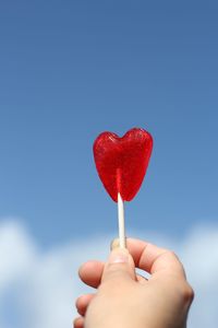 Close-up of hand holding heart shape lollipop against blue sky