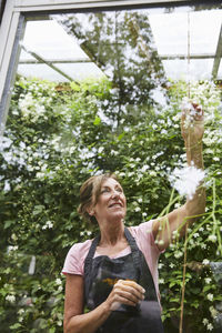 Smiling senior gardener analyzing plants seen through glass