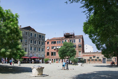 People on street by buildings in city against sky