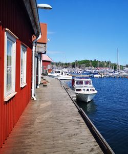 Sailboats moored on harbor by building against clear blue sky