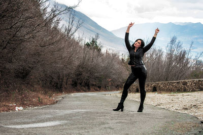 Full length of woman with arms raised standing on road