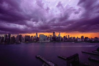 Modern buildings in city by river against cloudy sky during sunset