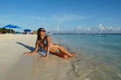Woman in bikini lying at beach against sky