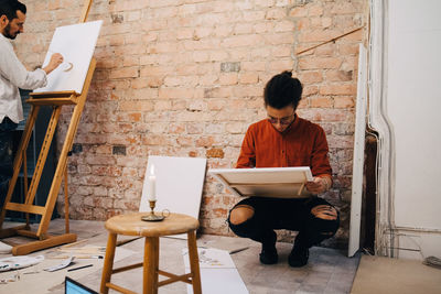 Serious male painters painting on canvas against brick wall at studio