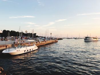 Sailboats moored in harbor at sunset