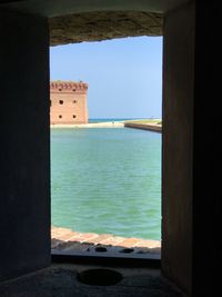 Buildings by sea against clear sky seen through window