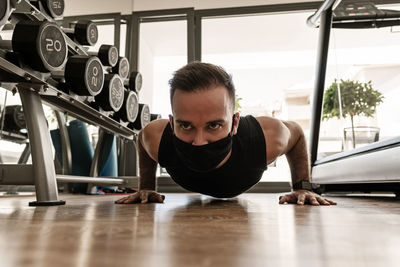 Surface level of man wearing mask exercising on floor at gym