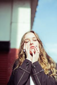 Young woman with eyes closed touching face during sunny day