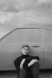 Portrait of young man sitting on car against sky