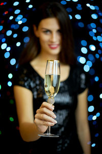 Portrait of beautiful young woman holding champagne flute against illuminated lights