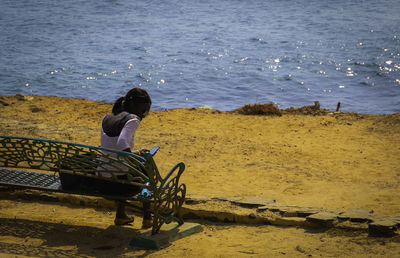 Young woman using smart phone while sitting on bench at beach