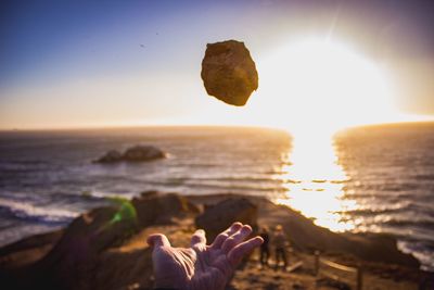 Close-up of person catching rock at beach against sky during sunset