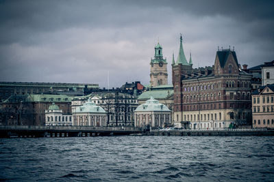 Buildings at waterfront against cloudy sky
