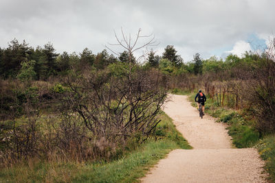 Man cycling through field against sky