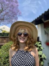 Portrait of smiling young woman wearing sunglasses and hat against sky