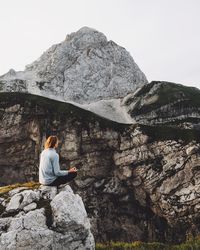 Rear view of woman sitting on rocky mountain against clear sky