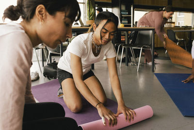 Non-binary business person rolling exercise mat by colleague at office