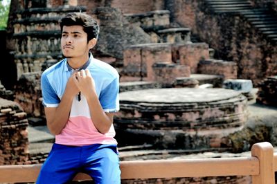 Thoughtful teenage boy sitting on railing against abandoned building