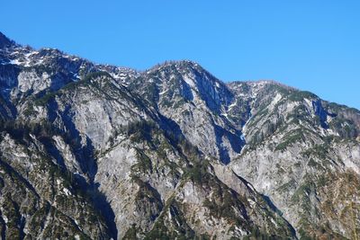 Low angle view of snowcapped mountains against clear blue sky