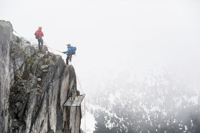 Climbers rappelling onto portaledge on a vertical cliff face.