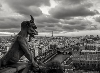 Demon statue and residential district against cloudy sky