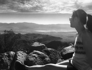 Man sitting on rock looking at mountains against sky