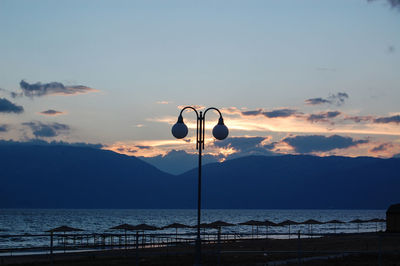 Street light by sea against sky during sunset