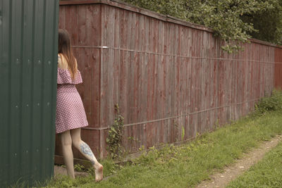 Woman standing by fence against plants