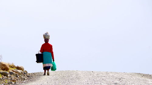 Rear view of woman walking on street against clear sky