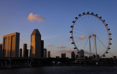 Ferris wheel by buildings against sky during sunset