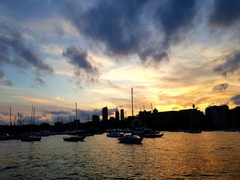 Silhouette boats in river by buildings against sky during sunset