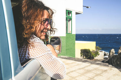 Close-up of woman sitting in car by sea against sky