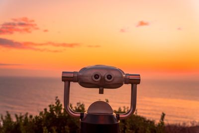 Close-up of coin-operated binoculars by sea against sky during sunset