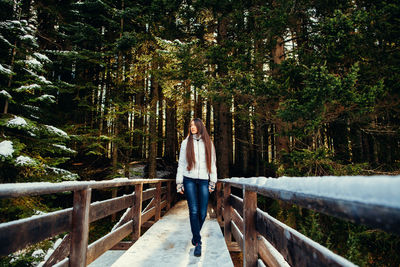 Full length of woman walking on snowy footbridge in forest