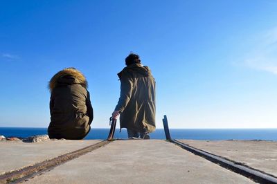 Rear view of man and woman wearing warm clothes while relaxing against sea