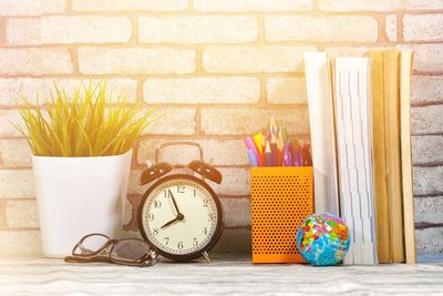 Close-up of potted plant with alarm clock and office supplies on table against wall