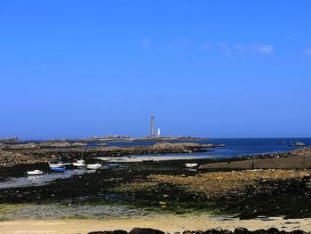 Lighthouse by sea against clear blue sky