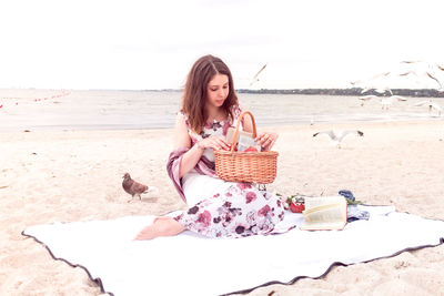 Young woman sitting on sand at beach against sky