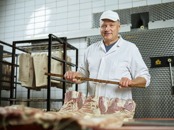 Smiling butcher with fresh raw meat standing in factory