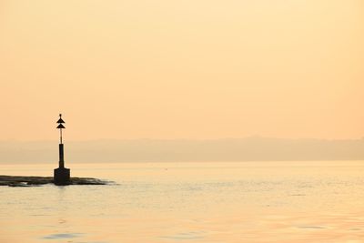 Silhouette lighthouse by sea against sky during sunset