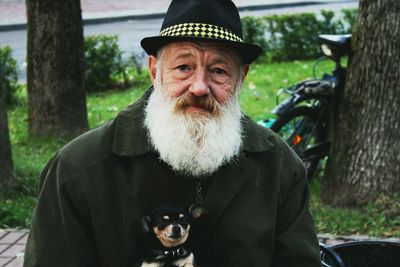 Portrait of mature bearded man with dog sitting in park