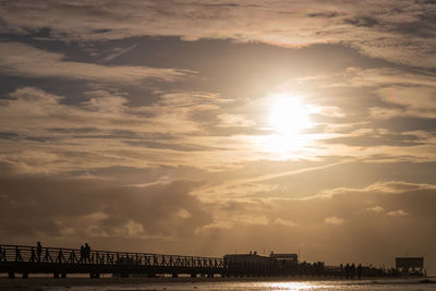 Silhouette pier over low tide wadden sea against sky during sunset