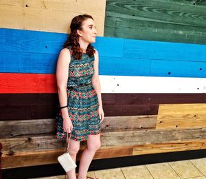 Full length of young woman standing by colorful wooden wall