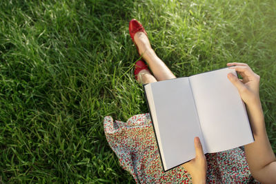 Low section of woman holding book on grassy field
