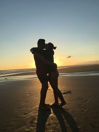 Side view of couple kissing at beach against sky during sunset