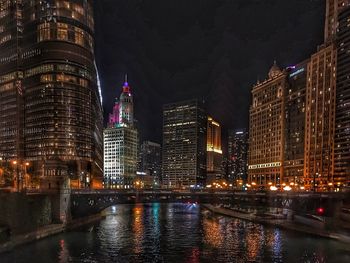 Illuminated buildings by river against sky at night