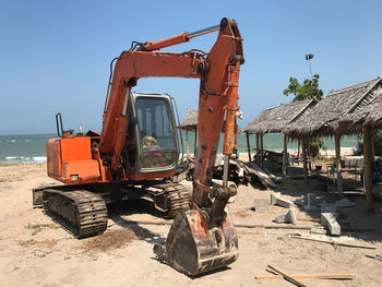 Construction vehicle by hut at beach against clear sky