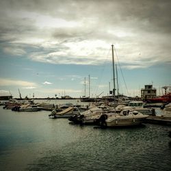 Boats in harbor against cloudy sky