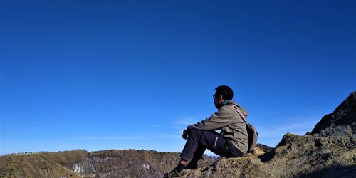 Man sitting on rock against clear blue sky