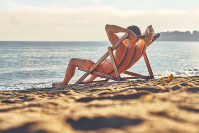 Deck chairs on shore at beach against sky